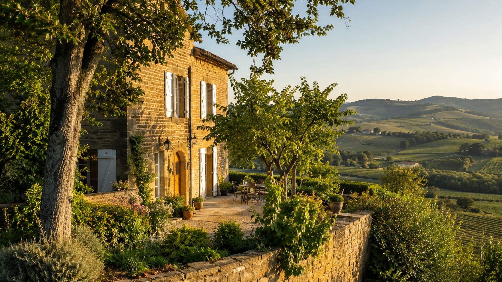 maison-pierre-doree-maloys-immobilier Maison traditionnelle en pierres dorées du Beaujolais, entourée d’un jardin verdoyant avec arbres et massifs fleuris. En arrière-plan, les collines couvertes de vignobles s’étendent sous une lumière dorée de fin d’après-midi, créant une atmosphère paisible et authentique.